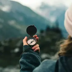 A person in a pink beanie holds a compass, navigating a misty mountain landscape. This symbolizes the journey of transition coaching.